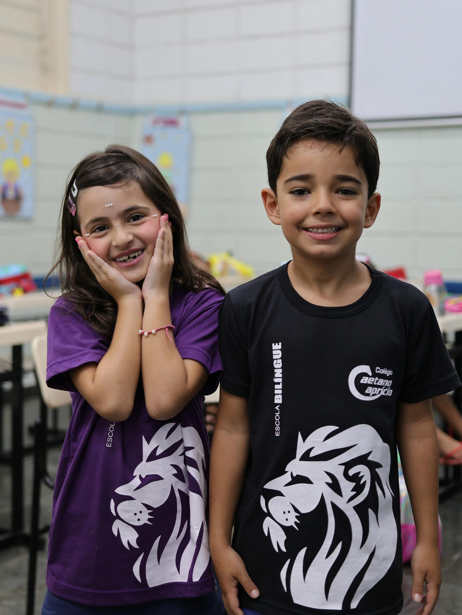 Dois alunos sorrindo, uniforme com o mascote leão da escola