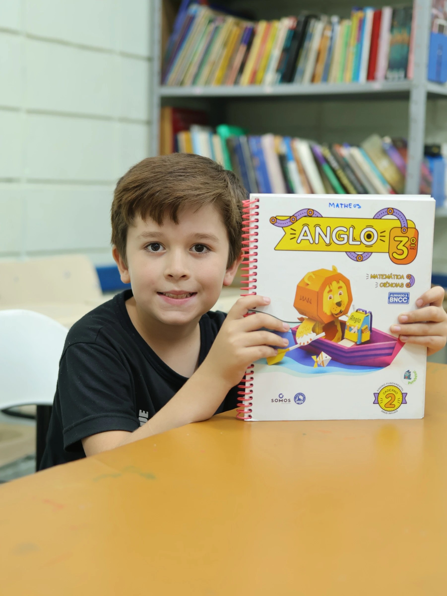 Aluno mostrando material do Sistema Anglo, sorrindo