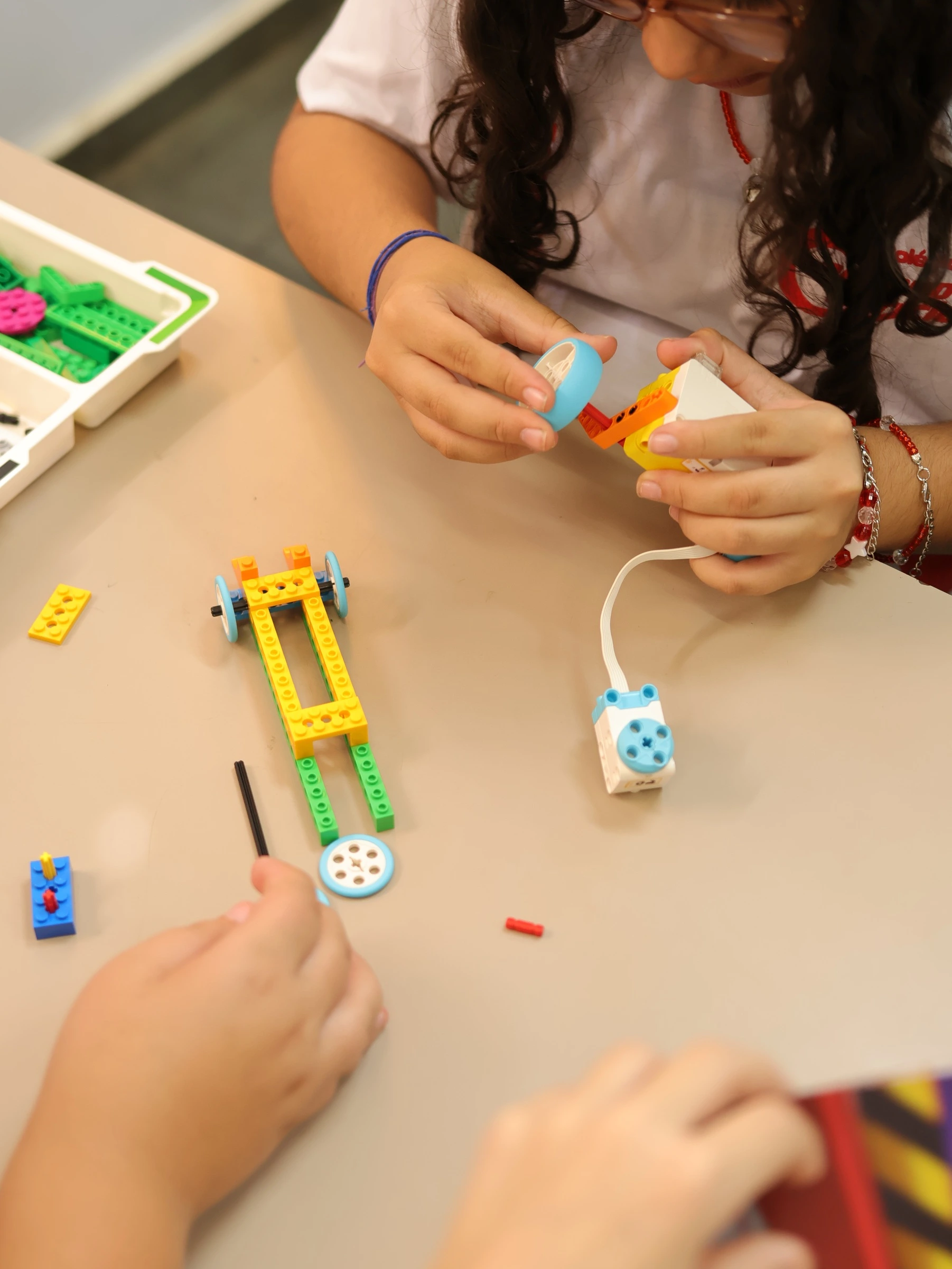 Mãos de alunos montando mecanismo com rodas em kit de robótica LEGO Education